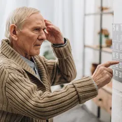 Älterer Mann mit Hand an der Stirn blickt auf Kalender. Ein Zeichen für Vergesslichkeit im Alter, wenn Daten verschwimmen.