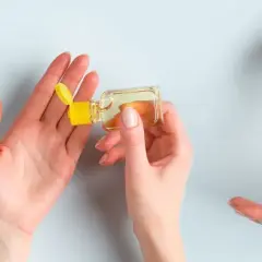 Dwie dłonie wykonują dezynfekcję rąk, jedna aplikuje płyn z buteleczki na drugą.