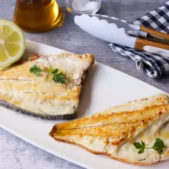 Dos filetes de dorada a la plancha, jugosos y dorados, servidos con perejil fresco y una rodaja de limón.