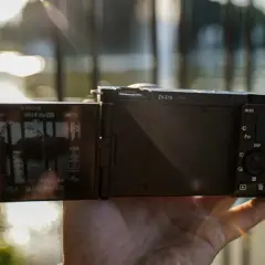 Dłoń trzyma aparat Sony Alpha ZV-E10 z uchylonym ekranem, na którym widać ustawienia nagrywania 4K.