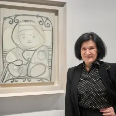 Mujer sonríe junto a un cuadro de un niño con paloma, en tonos grises y blancos.