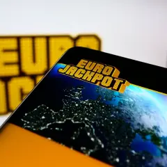 Logo Eurojackpot na ekranie telefonu z widokiem Europy nocą.