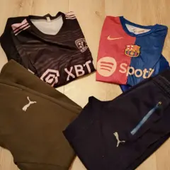 Dwa komplety odzieży piłkarskiej dla chłopca: czarna koszulka z różowymi pasami i herbem, niebiesko-czerwona koszulka FC Barcelony, brązowe i granatowe spodnie piłkarskie chłopięce z logo Pumy.