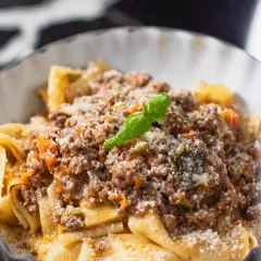 Un plat de pâtes fraîches, garni d'une sauce bolognaise riche et savoureuse, parsemé de parmesan et d'une feuille de basilic. Une recette spaghetti bolognaise italienne authentique.