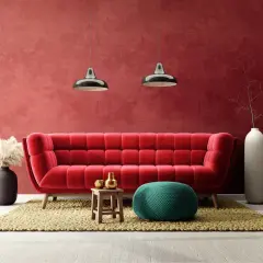 Soggiorno moderno con divano rosso vellutato e **effetto spugnato muro** color bordeaux. Due lampade a sospensione, pouf verde acqua e vasi bianchi completano l'arredo.