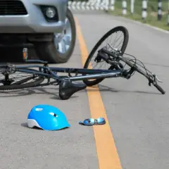 Samochód nie ustąpił pierwszeństwa rowerzyście. Na drodze leży przewrócony rower, niebieski kask i okulary.