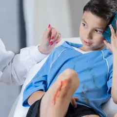 Niño con golpe en la cabeza, recibe atención médica. Tiene una compresa fría en la sien y una herida en la rodilla.