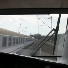 Widok z kabiny maszynisty na mijający pociąg. Widać tory, sieć trakcyjną i niebo z chmurami.