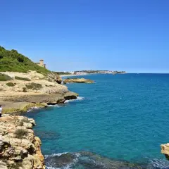 Dos personas caminan por el camí de ronda en Tarragona, disfrutando de las vistas al mar Mediterráneo y la costa.