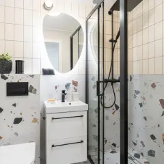 Nowoczesna łazienka tanim kosztem inspiracje: biała szafka, czarna armatura, lustro z podświetleniem i płytki imitujące terrazzo.