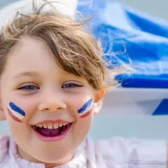 Uśmiechnięta Agnieszka z francuskimi barwami na policzkach, trzymająca flagę Francji.