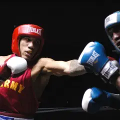 Two boxers, one in red with "ARMY" on his vest, the other in blue, engage in intense **sparring**. Their gloves are raised, ready for the next move in this practice bout.