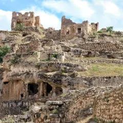 Ruiny starożytnego miasta Hasankeyf na skalistym zboczu, z widocznymi jaskiniami i kamiennymi murami.