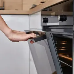 Ręce otwierają piekarnik Amica. Widać pokrętło temperatury i oznaczenia funkcji.