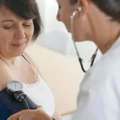 Lekarka bada ciśnienie pacjentce. Na ramieniu kobiety widoczny jest mankiet ciśnieniomierza, a lekarz słucha stetoskopem.