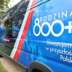 Niebieski bus z napisem "RODZINA 800+" i hasłem "Inwestujemy w przyszłość Polski". Obok rodziny, symbolizującej program 800 plus zmiany.