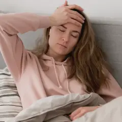 En kvinna med handen på pannan i sängen, känner ångest på morgonen.