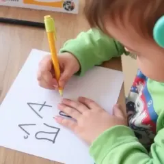 Dziecko z zielonymi słuchawkami ćwiczy pisanie, by pokonać dysgrafię. Na kartce widać litery.