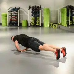 Mężczyzna wykonuje pompki diamentowe na siłowni, ćwicząc klatkę piersiową i triceps.