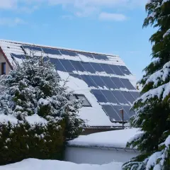 Schneebedeckte Solaranlage auf einem Hausdach, die zeigt, wie man im Winter heizen kann.