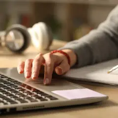 Personens händer arbetar vid en laptop och skriver i en anteckningsbok. Perfekt för kreativt skrivande distans.