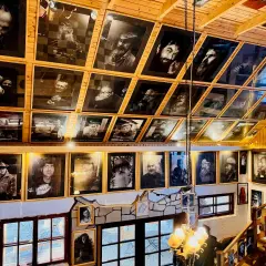 Wnętrze z licznymi czarno-białymi portretami, tworzącymi siekierozada cisna historia. Drewniane ściany i sufit podkreślają artystyczny klimat.