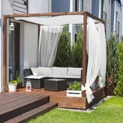 Drewniana pergola z białymi zasłonami to idealne miejsce na tarasie. Zapewnia cień i prywatność, a także stanowi stylowe tło dla mebli ogrodowych.