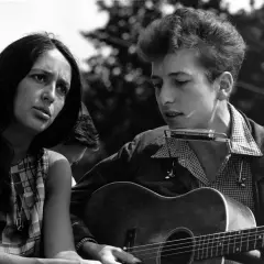 Młody Bob Dylan gra na gitarze i harmonijce, obok siedzi kobieta. To obraz z czasów, gdy jego twórczość zasłużyła na nagrodę Nobla.