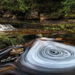 Wodospad w lesie, gdzie woda tworzy wiry. Efekt długiej ekspozycji, jakby użyto filtrów fotograficznych.
