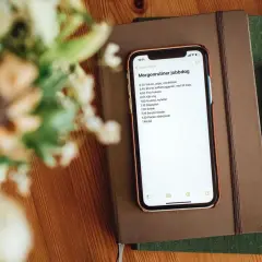 iPhone displaying a morning routine list on top of notebooks with a pen and flowers.