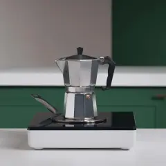 En mokkakanne står på en induksjonshäll, redo för att brygga kokkaffe.
