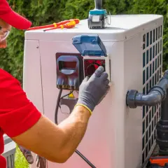 Technik w rękawiczkach sprawdza panel pompy ciepła, by zapewnić optymalną, jaką temperaturę daje pompa ciepła. Narzędzia leżą obok.