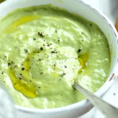 A bowl of creamy green basil pesto with olive oil and cracked pepper, served with toasted bread.