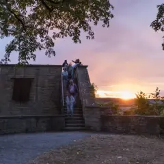 Menschen steigen die Treppen zum schlosskeller herrenberg hinauf, während die Sonne bei einem dramatischen Abendhimmel untergeht.