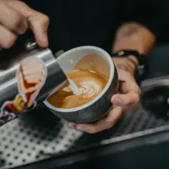 Barista tworzy wzorek na kawie, nalewając spienione mleko. To prosty sposób, jak zrobić wzorek na kawie.