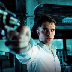 Robert Pattinson i en vit skjorta siktar med en pistol i en mörk, mystisk scen, typisk för hans filmer.