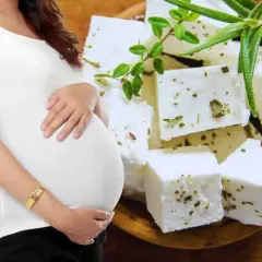 Pancia di donna incinta accarezzata, con cubetti di feta aromatizzata alle erbe sullo sfondo.