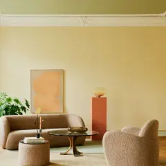 Sanfte gelbe Wände mit einer dezenten Streichtechnik Wand, kombiniert mit einem grünen Deckenanstrich, schaffen eine warme Atmosphäre. Ein beiger Bouclé-Sofa und Sessel laden zum Entspannen ein.