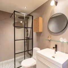 Modernt badrum med duschhörna i glas, toalett och kommod. Väggarna är klädda i stilren microcement.