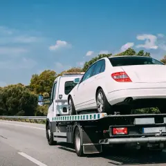 Laweta holująca biały samochód osobowy na autostradzie.
