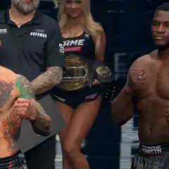 Dwóch zawodników MMA, jeden z tatuażami na klatce piersiowej, gotowych do walki. W tle ring girl z pasem mistrzowskim FAME. Wyniki walki będą emocjonujące!