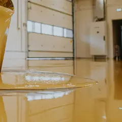 Liquido giallo, probabilmente resina epossidica cos'è, cola da un secchio su un pavimento lucido in un capannone.