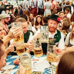 Ludzie w tradycyjnych strojach bawią się na Oktoberfest, wznosząc kufle piwa.