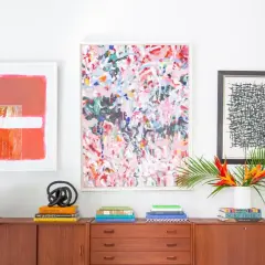 Vibrant abstract art and graphic prints adorn a wall above a midcentury credenza, showcasing a stylish blend of midcentury graphic design.