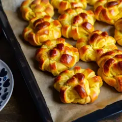 Nybakade zeina saffransbullar på en plåt, gyllene och inbjudande. En skål med socker och en röd duk anas i bakgrunden.