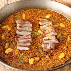 Arroz con secreto de cerdo, jugoso y dorado, con trozos de carne y verduras en una paellera.