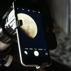 Aparat telefoniczny zamocowany do teleskopu, gotowy do astrofotografii smartfonem. Na ekranie widoczny Księżyc.