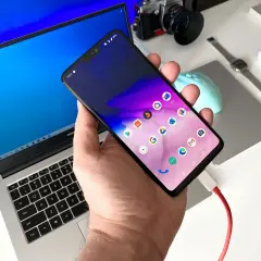 Ręka trzyma smartfon podłączony kablem do laptopa. To pokazuje, jak przenieść zdjęcia z telefonu na telefon, korzystając z komputera.