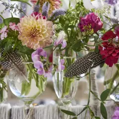 Moderne tischdeko blumen: Dahlien, Rosen und Margeriten in Glasvasen, dekoriert mit Federn.