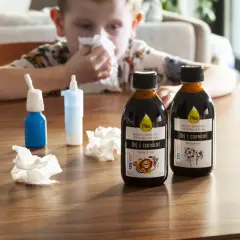 Chłopiec z chusteczką przy nosie, obok butelki oleju z czarnuszki – naturalne sposoby na alergię.